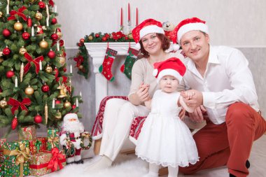 Noel ve yeni yıl kutlama. Üç Kişilik xmas hediye ile Noel ağacı yakınındaki neşeli genç aile portresi. Arka plan üzerinde Noel çorap ile bir şömine. İyi Bayramlar