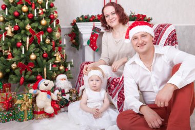 Noel ve yeni yıl kutlama. Üç Kişilik xmas hediye ile Noel ağacı yakınındaki neşeli genç aile portresi. Arka plan üzerinde Noel çorap ile bir şömine. İyi Bayramlar