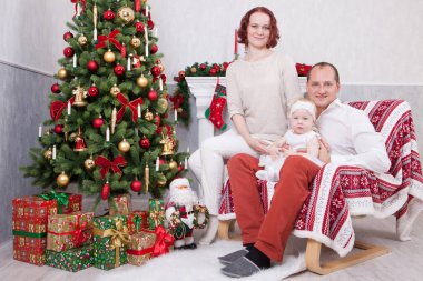 Noel ve yeni yıl kutlama. Üç Kişilik xmas hediye ile Noel ağacı yakınındaki neşeli genç aile portresi. Arka plan üzerinde Noel çorap ile bir şömine. İyi Bayramlar