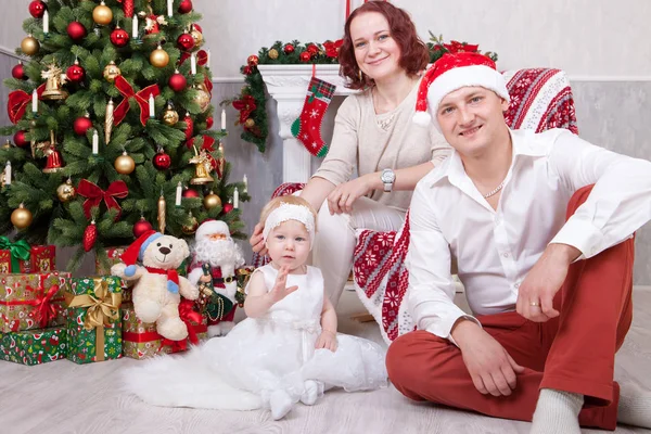 Celebración de Navidad o Año Nuevo. Retrato de alegre familia joven de tres personas cerca del árbol de Navidad con regalos de Navidad. Una chimenea con medias de Navidad en el fondo. Felices fiestas — Foto de Stock