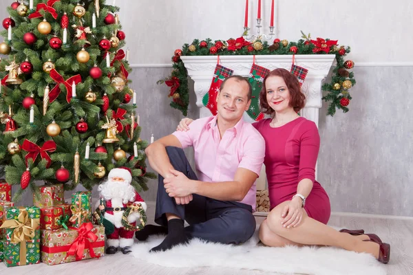 Рождество или Новый год. Молодая пара сидит и обнимается в рождественском интерьере, рядом с камином, елкой. С праздником! — стоковое фото