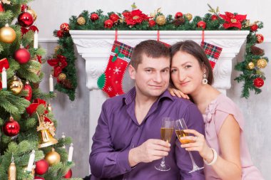 Noel ve yeni yıl kutlama. Genç güzel çift bardak şampanya Noel ile. Bir şömine arka plan üzerinde Noel çorap ile