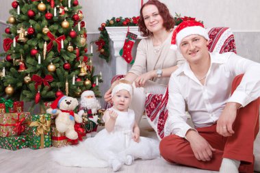 Noel ve yeni yıl kutlama. Üç Kişilik xmas hediye ile Noel ağacı yakınındaki neşeli genç aile portresi. Arka plan üzerinde Noel çorap ile bir şömine. İyi Bayramlar