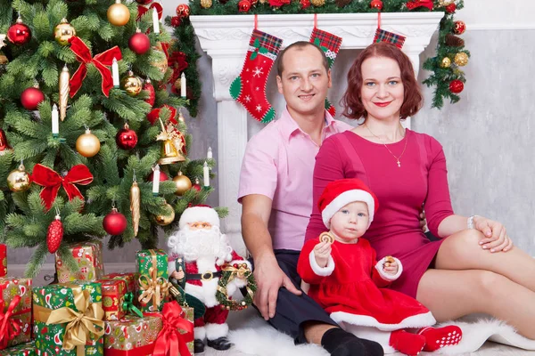 Celebración de Navidad o Año Nuevo. Feliz familia joven sentada cerca del árbol de Navidad con regalos de Navidad. Una chimenea con medias de Navidad en el fondo — Foto de Stock