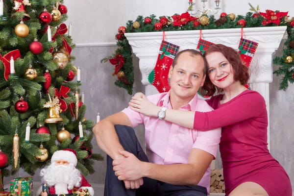 Рождество или Новый год. Молодая пара сидит и обнимается в рождественском интерьере, рядом с камином, елкой. С праздником! — стоковое фото