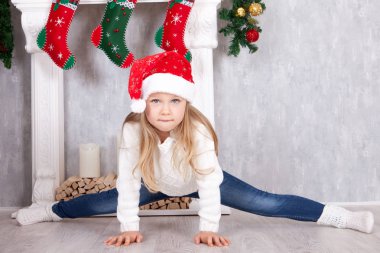 Jimnastik poz, streç. Santa şapkalı küçük sarışın kız çapraz-sicim egzersiz yapıyor. Noel iç tam bir split yapmak