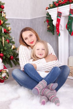Noel ve yeni yıl kutlama. Xmas hediye Noel ağacının yanında oturan kızı kucaklama ile mutlu genç anne. Bir şömine arka plan üzerinde Noel çorap ile