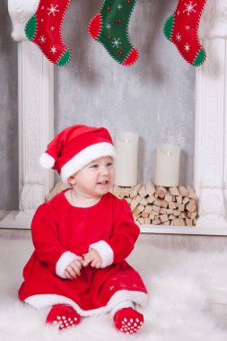 Noel ya da Yeni Yıl kutlaması. Küçük kız elf ve santa şapka kırmızı bir festival takım elbise giymiş, hediyeler ile Noel ağacının yakınında yere oturur. Arka planda noel çorabı olan bir şömine