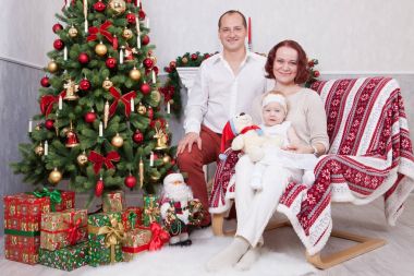 Noel ve yeni yıl kutlama. Üç Kişilik xmas hediye ile Noel ağacı yakınındaki neşeli genç aile portresi. Arka plan üzerinde Noel çorap ile bir şömine. İyi Bayramlar