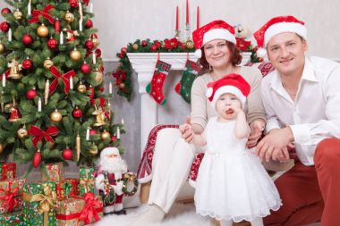 Noel ve yeni yıl kutlama. Üç Kişilik xmas hediye ile Noel ağacı yakınındaki neşeli genç aile portresi. Arka plan üzerinde Noel çorap ile bir şömine. İyi Bayramlar