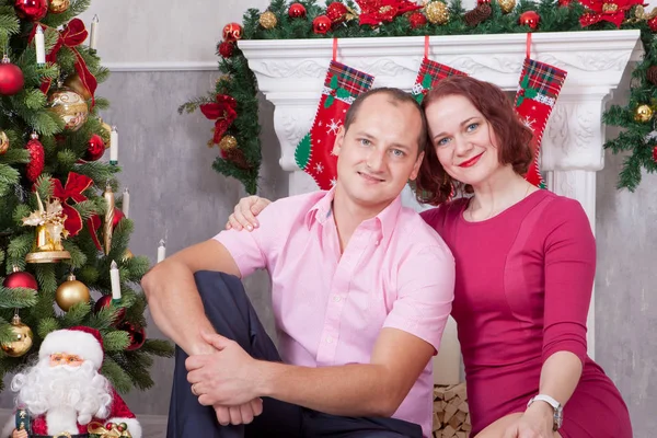 Celebración de Navidad o Año Nuevo. Pareja joven sentarse y abrazar en el interior de Navidad, cerca de la chimenea, árbol de Navidad. Felices fiestas — Foto de Stock