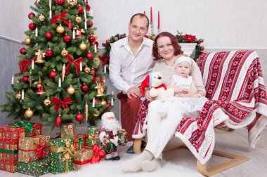 Noel ve yeni yıl kutlama. Üç Kişilik xmas hediye ile Noel ağacı yakınındaki neşeli genç aile portresi. Arka plan üzerinde Noel çorap ile bir şömine. İyi Bayramlar