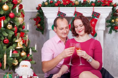 Noel ve yeni yıl kutlama. Genç güzel bir kadeh şampanya ile xmas hediye Noel ağacının yanında oturan çift. Arka plan üzerinde Noel çorap ile bir şömine. İyi Bayramlar