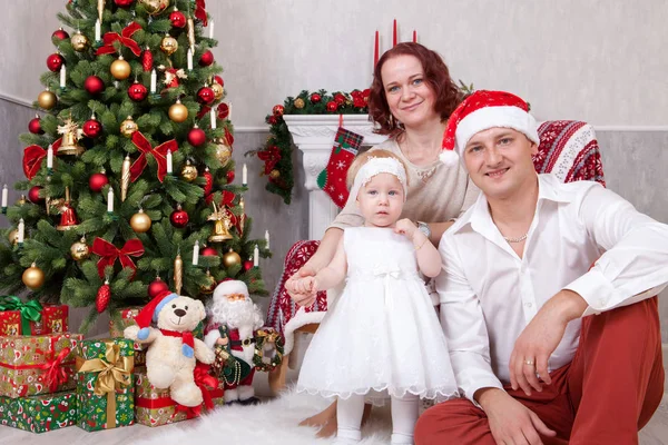 Celebración de Navidad o Año Nuevo. Retrato de alegre familia joven de tres personas cerca del árbol de Navidad con regalos de Navidad. Una chimenea con medias de Navidad en el fondo. Felices fiestas — Foto de Stock