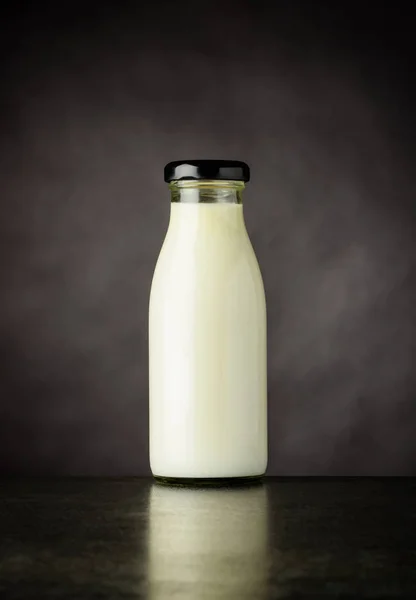 Kleine Glasflasche mit Milch auf dunklem Hintergrund — Stockfoto