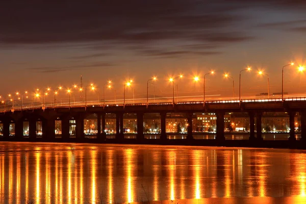 Ponte sul fiume Dnieper la sera. La luce delle lanterne si riflette nel ghiaccio ghiacciato . — Foto Stock