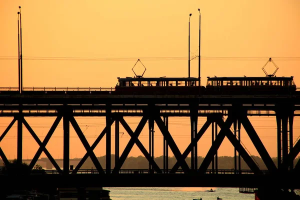 Silhouettes d'un pont à deux niveaux et 2 tramways sur fond de coucher de soleil — Photo
