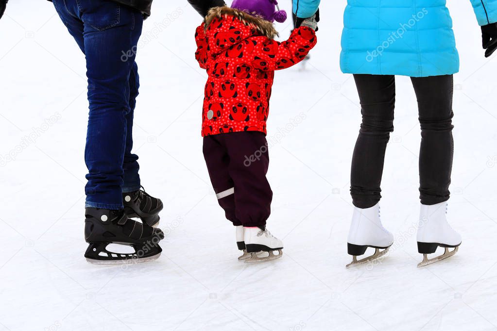 Little child skates with his parents at the ice rink in winter. A man and woman is teaching her child to skate. Sports clubs, active family sport, winter holidays