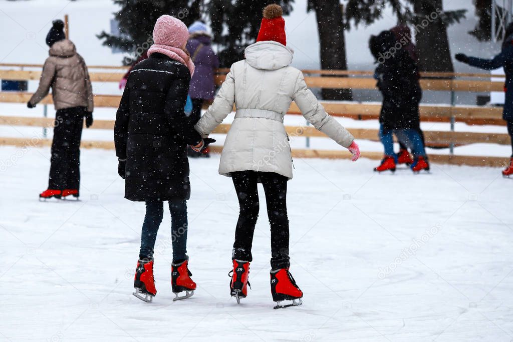 Winter ice rink. The girls in the red skate riding on the ice. Active family sport during the children s  winter holidays and the cold season. School sports clubs
