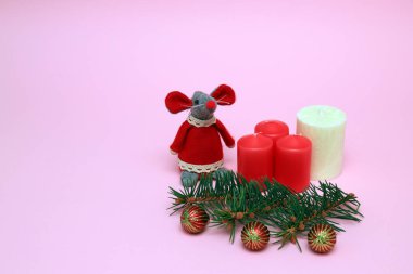 Funny toy red mouse, the symbol of the Chinese New Year 2020 on a pink background, red, white candles, balls, Christmas tree branches. Space for text