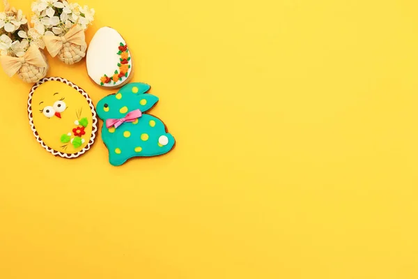 Handmade multi-colored gingerbread cookies in the form of a bunny and Easter eggs, straw shoes and flowers on a yellow background. Gingerbread Easter rabbit, decoration — Stock Photo, Image