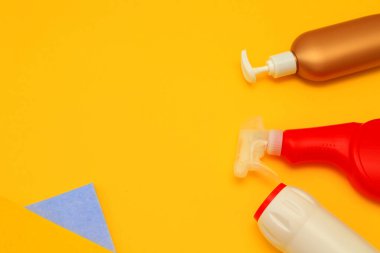 Mutfağı ve banyoyu temizlemek için sarı arka planda plastik yıkama kapları, peçeteler, süngerler. Deterjanlar, temizlik şişeleri, çeşitli boylar, renkler..