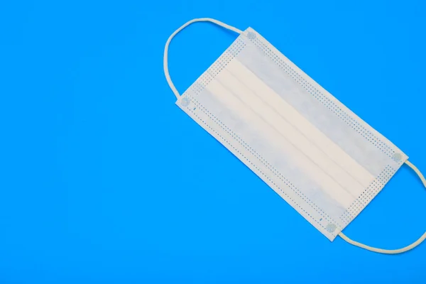 Protective medical disposable mask. White face mask, protection against viruses and bacteria, on a blue background, close-up, for quarantine during a coronavirus pandemic covid-19