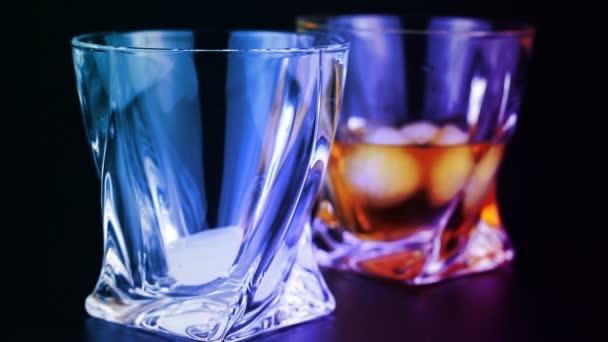 Whisky se vierte en un vaso con hielo sobre un fondo negro — Vídeo de stock