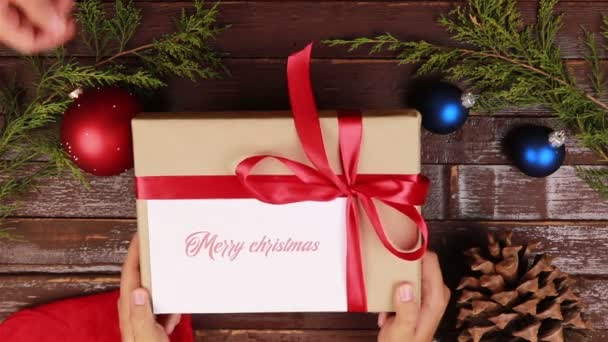 Top view hands gives a gift with the inscription Merry Christmas at wooden desk — Stock Video