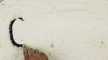 Genç adam bir kelime gluten üstü çizili beyaz un üzerinde yazıyor.