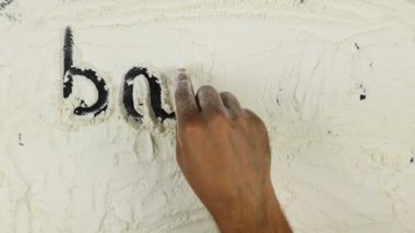 Genç adam bir kelime Pastane Dükkanı beyaz un üzerinde yazıyor.