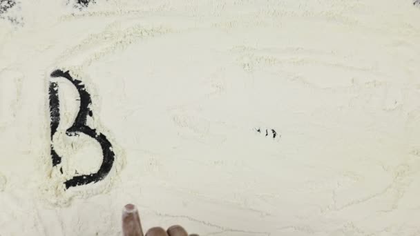 Young man writes a word baking on white flour — Αρχείο Βίντεο