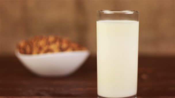 Glas Milch und Kekse im Teller auf einem Holztisch und braunem Hintergrund — Stockvideo