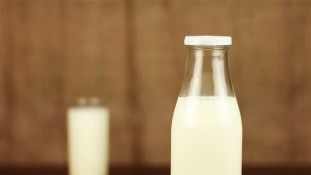 Una bottiglia di latte e un bicchiere di latte su un tavolo di legno e sfondo marrone — Video Stock