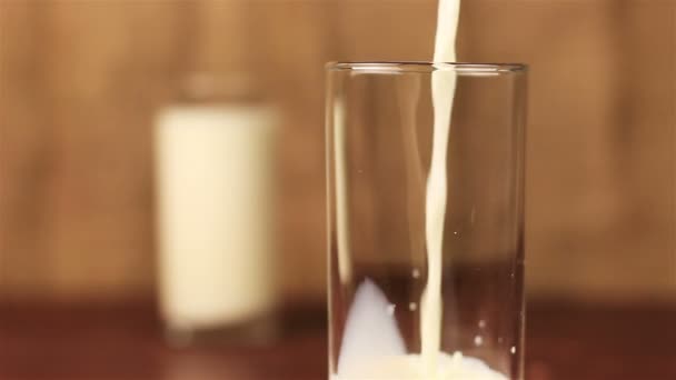 Молоко наливається в склянку на дерев'яний стіл і коричневий фон — стокове відео