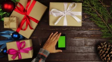 Üstten Görünüm ellerini kullanarak cep telefonu dokunmatik multi dokunmatik jestleri yeşil ekran Noel ahşap masa üzerinde