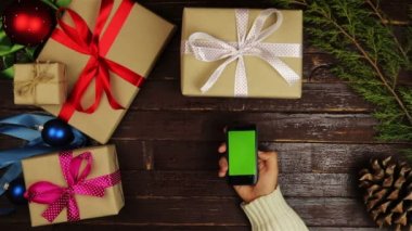 Üstten Görünüm ellerini kullanarak cep telefonu dokunmatik multi dokunmatik jestleri yeşil ekran Noel ahşap masa üzerinde
