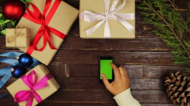 Üstten Görünüm ellerini kullanarak cep telefonu dokunmatik multi dokunmatik jestleri yeşil ekran Noel ahşap masa üzerinde