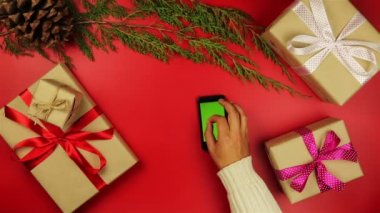 Üstten Görünüm Noel eller dokunmatik ekran smartphone kullanarak alışveriş listesi yukarıda kırmızı zemin üzerine kahve içme Noel hediyelerini tablet.