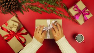 Üstten Görünüm eller yukarıda kırmızı zemin üzerine çıkartıyorum Noel hediyeleri. Hediye kahverengi kağıt sarılı ve beyaz birbant bağlamıştım