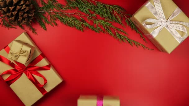 Το Top view χέρια κρατώντας χριστουγεννιάτικα δώρα σε κόκκινο φόντο από πάνω. Δώρο τυλιγμένο σε καφέ χαρτί και δεμένα μωβ κορδέλα — Αρχείο Βίντεο