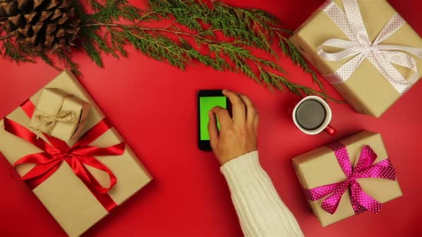 Bovenaanzicht handen met behulp van de mobiele telefoon touchscreen multi touch gebaren groen scherm op Kerstmis rode achtergrond van bovenaf. — Stockvideo