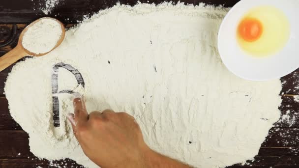 Widok z góry młody człowiek pisze słowo pieczenia na białej mąki na biurko z drewna z góry. — Wideo stockowe