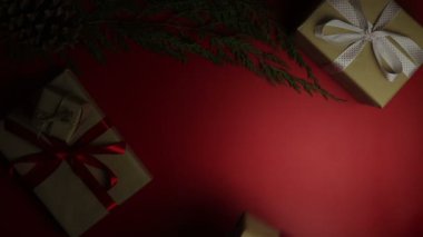Üstten Görünüm yukarıdan kırmızı arka plan üzerinde Noel hediyeleri tutan eller. Hediye kahverengi kağıt sarılı ve mor kurdele bağlanmış