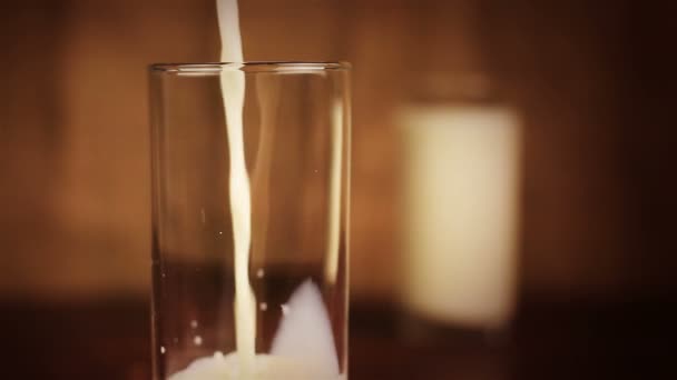 Milk pouring into glass on a wooden table and brown background — Stock Video