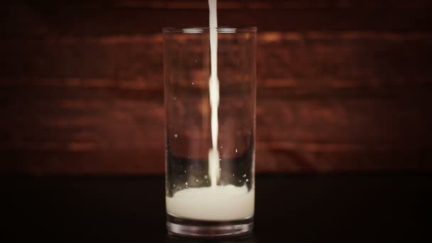 Leche vertiendo en un vaso sobre un fondo de madera — Vídeos de Stock