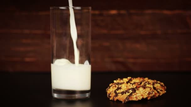 Milk pouring into glass and cookies on wooden background — Stock Video