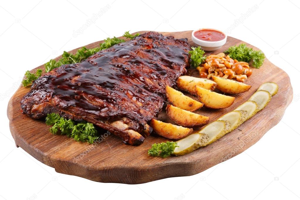 Meat grilled ribs on a white background, on a board with baked potatoes, cucumbers and pickled mushrooms