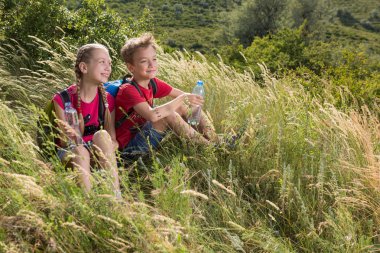 Erkek ve kız yüksek otların arasında oturan ve su şişeleri holding