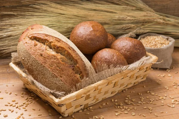 Assortment of fresh bread in a basket on a wooden table, composition with additional accessories — Stock Photo, Image